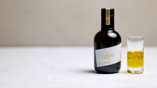 high polyphenol olive oil in a dark glass bottle next to a shot of extra virgin olive oil showing the rich deep colour of pure olive oil.