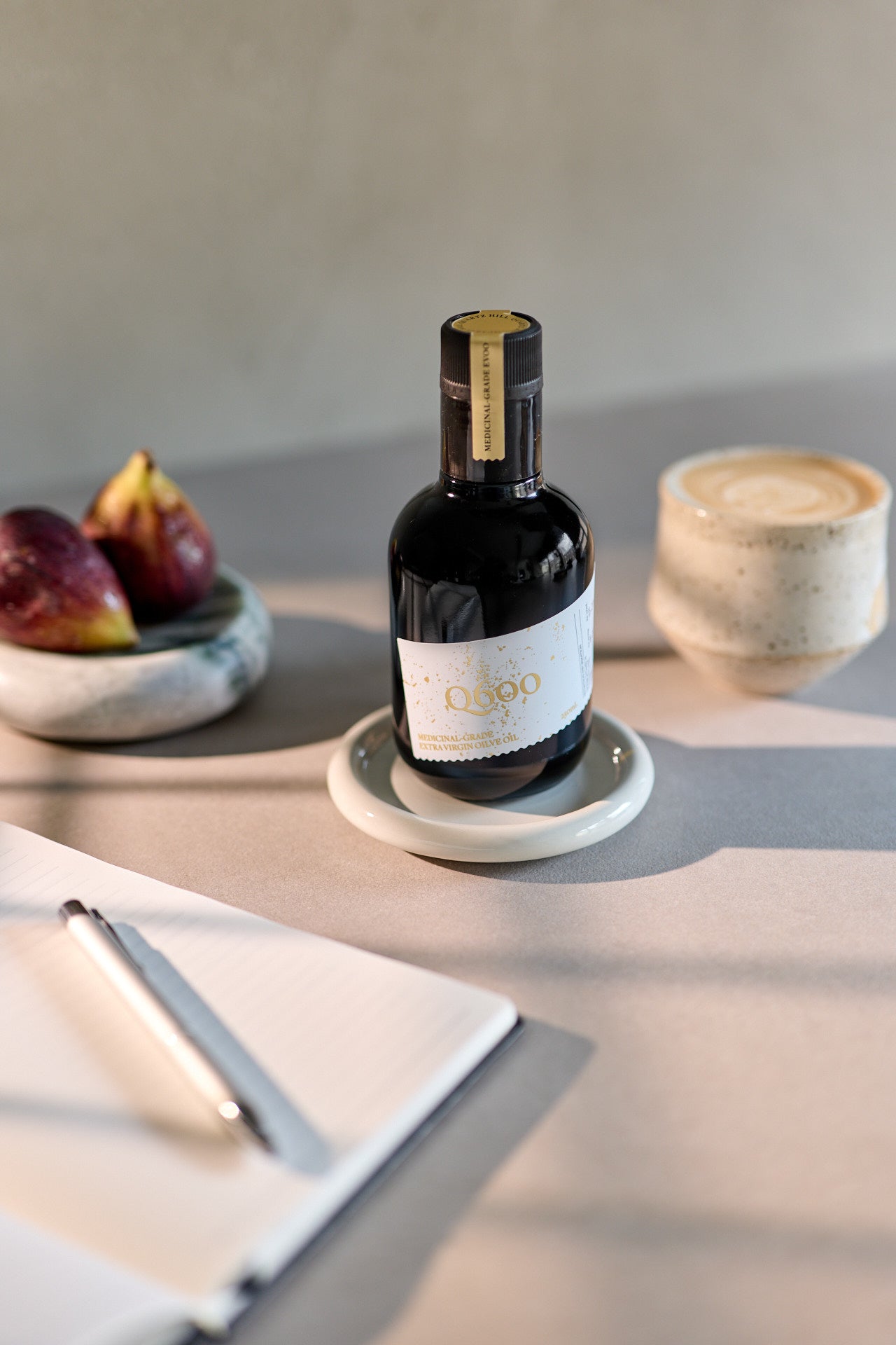 Morning coffee with a shot of olive oil next to some fresh figs and a journal for daily routine.