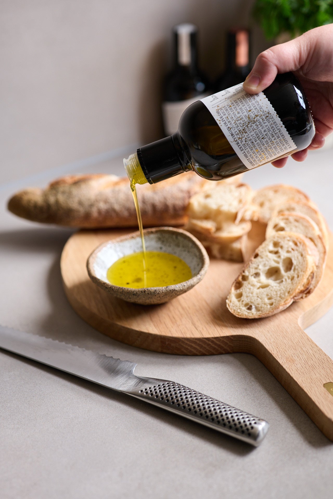 Person pouring early harvest Australian olive oil from a bottle into a small bowl on a wooden cutting board with bread.