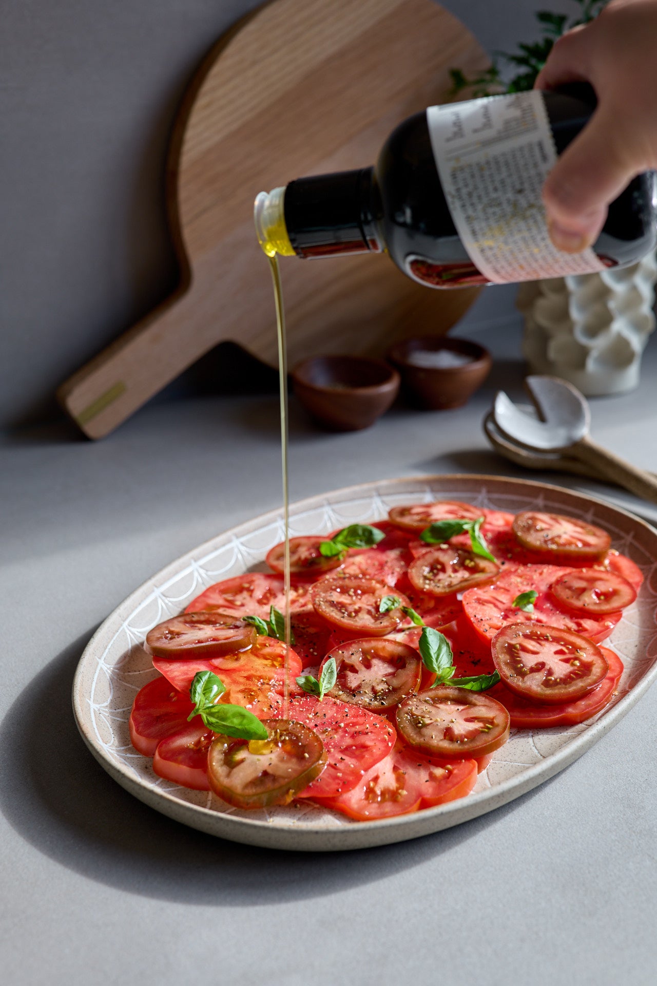 Tomato salad on a plate with a hand pouring high polyphenol olive oil over it.