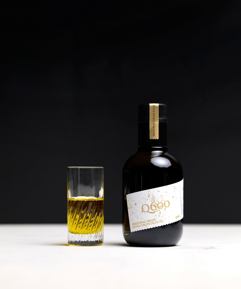 medicinal grade polyphenol extra virgin olive oil in a black glass with daily shot glass showing the liquid gold olive oil colour of 100% pure olive oil.