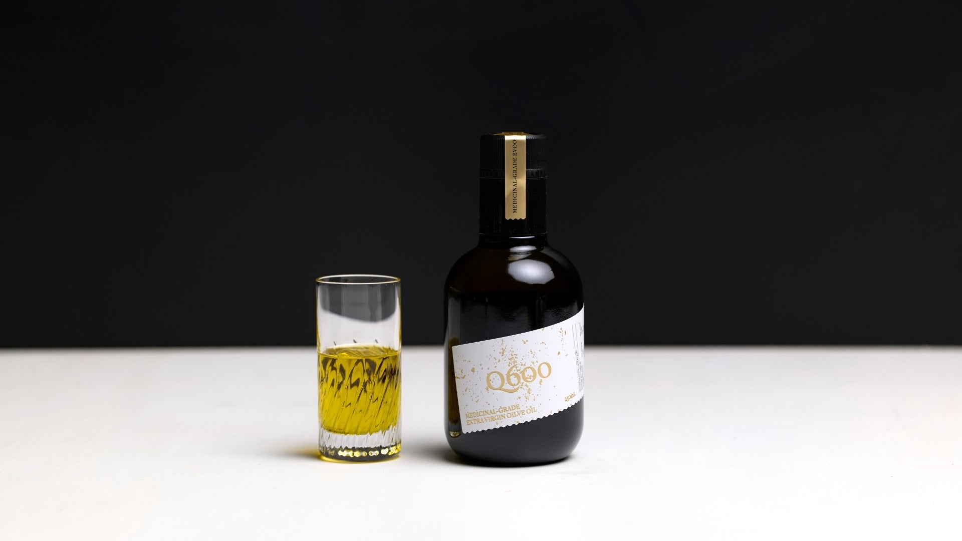 medicinal grade polyphenol extra virgin olive oil in a black glass with daily shot glass showing the liquid gold olive oil colour of 100% pure olive oil.
