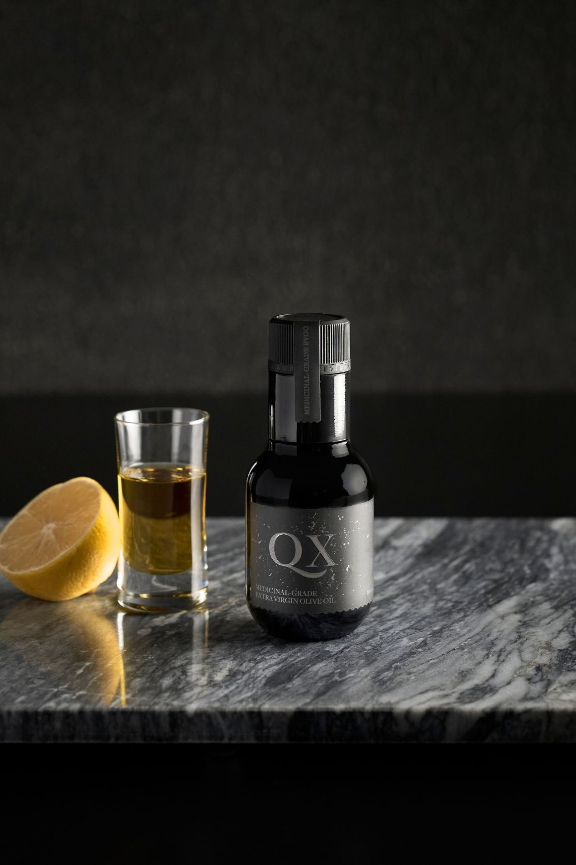 black glass bottle of EVOO with lemon next to a daily olive oil shot containing australia's highest polyphenol oil.