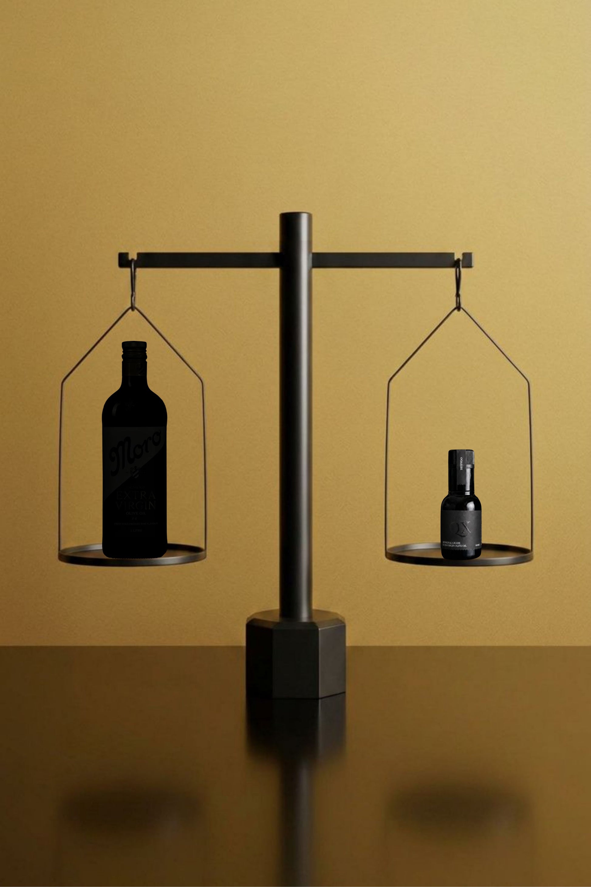 A minimalist black metal balance scale with two hanging trays, one holding a dark bottle of olive oil and the other holding a smaller dark bottle of qx olive, set against a warm golden background. Depicting the difference in concentration of the smaller bottle that not as much is required for a daily dose of polyphenols.